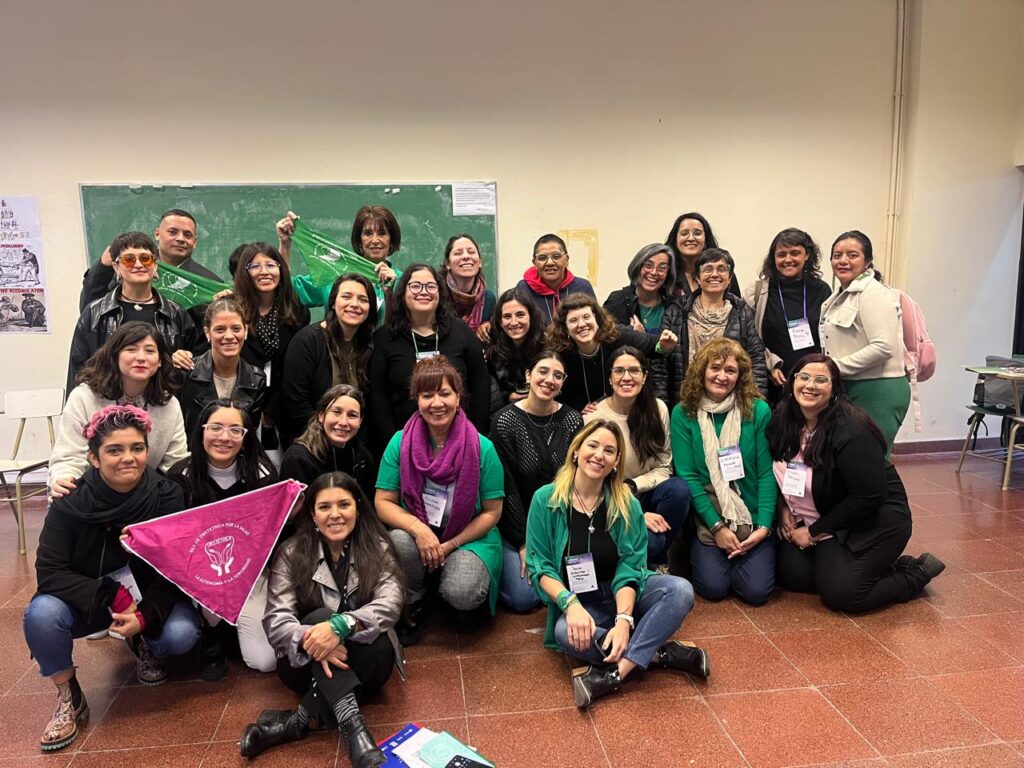 Grupo de 25 obstétricas posa para la foto. La mayoría viste de verde y una de ellas sostiene un pañuelo color magenta, que identifica la lucha de las obstétricas de capital federal para lograr una ley que actualice la regulación de su ejercicio profesional.